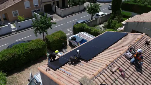 Des techniciens solaires posant des panneaux sur une maison avec harnais de sécurité.